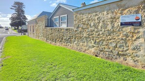 A stone wall with a cottage, a grassy lawn, and a clear sky. - Cornerstone Cottage - Historic 1850's Cottage Pets Welcome - Inside by neg (Robe)