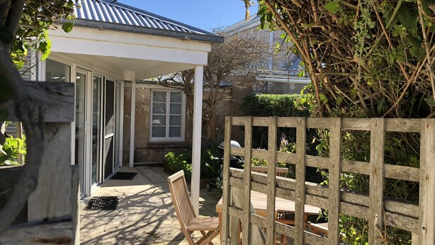 A covered patio area with a wooden fence, a wooden chair, and a table. - Cornerstone Cottage - Historic 1850's Cottage Pets Welcome - Inside by neg (Robe)