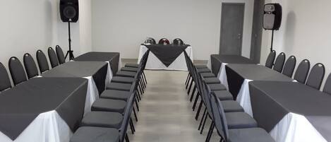 A conference room with a long table, chairs, and two speakers.