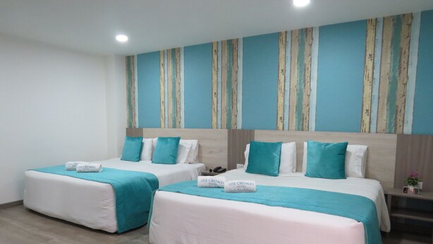 Une chambre d’hôtel avec deux lits, chacun recouvert d’une courtepointe et doté d’oreillers de couleur turquoise, et agrémentée d’une tête de lit en bois.