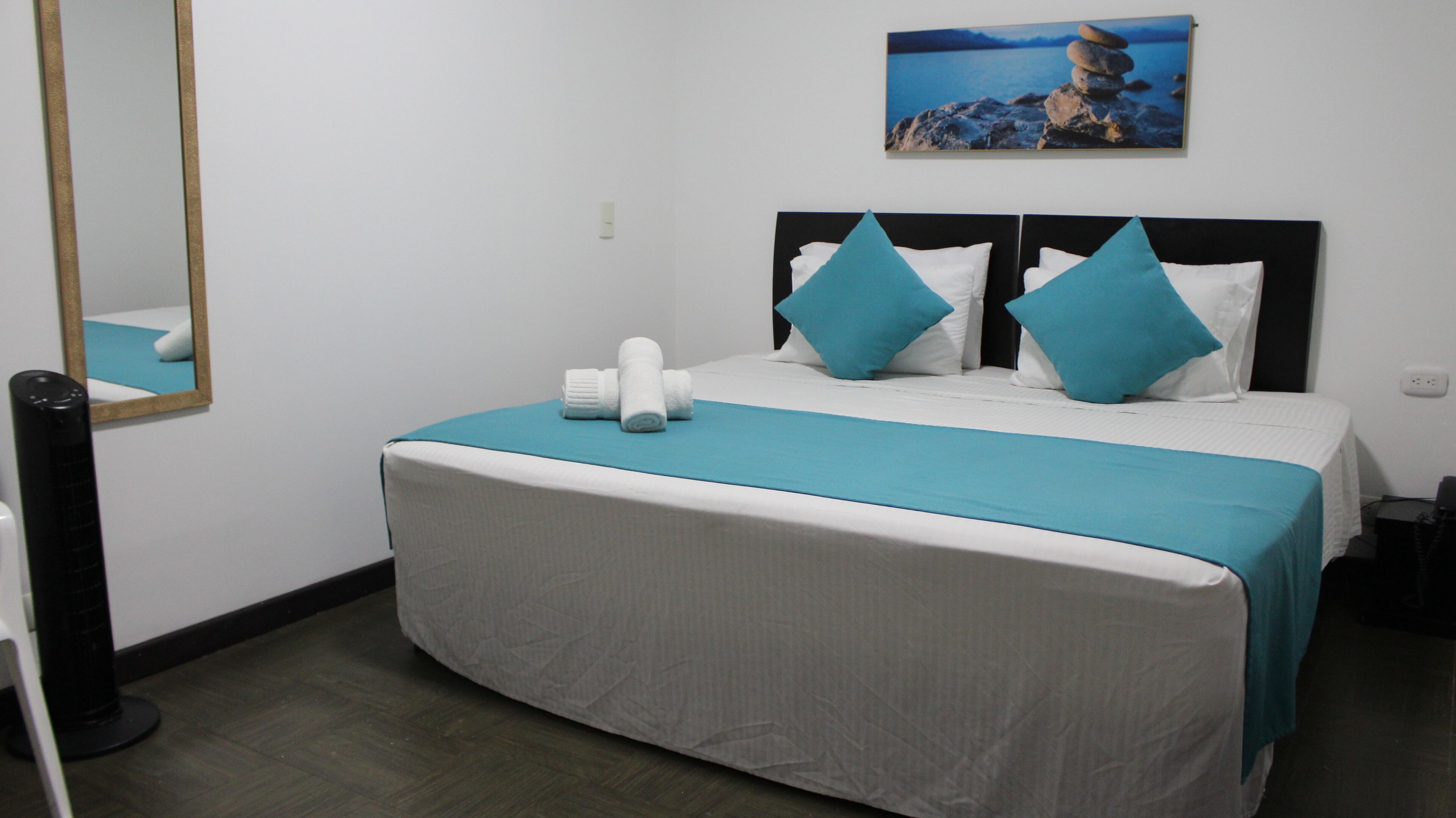 Una habitación de hotel con cama, espejo, cuadro y calefactor.