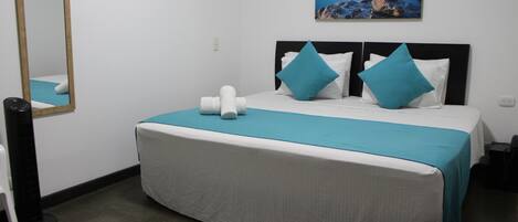 Quarto de hotel com cama, espelho, quadro e aquecedor.