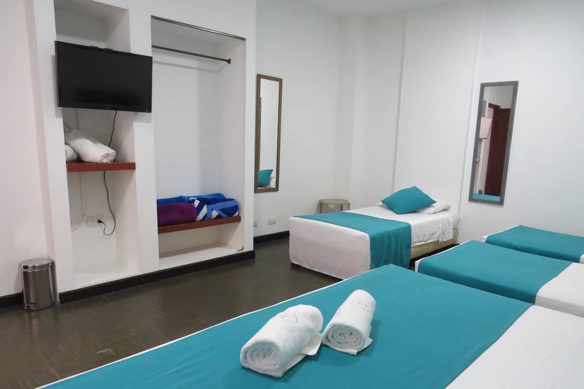A hotel room with two beds, a TV, a mirror, and a shelf with towels.
