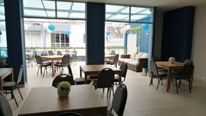 Un vaste espace de restauration intérieur, doté de nombreuses tables et chaises, de grandes fenêtres et offrant une vue sur la terrasse extérieure.