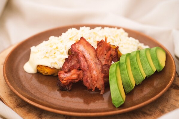 A plate with scrambled eggs, bacon, and avocado slices.