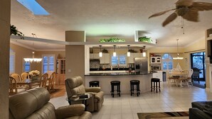 Een ruime woonkamer met hoge plafonds, een eethoek, een keuken met moderne apparatuur en een open haard.