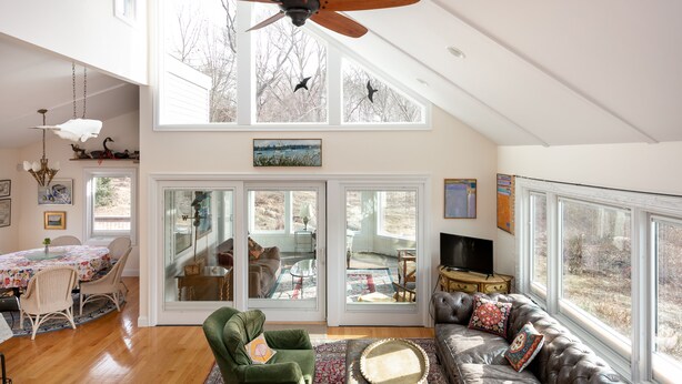 Un salón amplio con techo alto, ventanas grandes, ventilador de techo y una zona de estar acogedora.