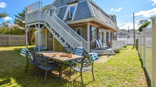 A house with a prominent staircase leading to a deck, a patio with a table and chairs, and a fenced backyard. - 400 Yards to the Beach! Dogs Welcome! (Dennis Port)