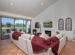 Ein großzügiges Wohnzimmer mit einem großen Fenster, einem Kamin und Blick auf einen Golfplatz.
