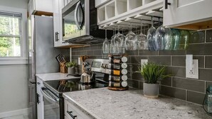 Una cocina moderna con armarios blancos, un refrigerador de acero inoxidable, un horno empotrado y una encimera con una cafetera y una planta.