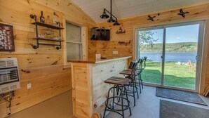 Un interior de madera con una zona de bar, sillas y vistas a un lago.