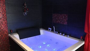 A large, rectangular bathtub with a digital display and a control panel, surrounded by dark tiled walls and a red curtain. - Suite Rouge Passion avec jacuzzi privatif en Provence (Plan-d'Orgon)