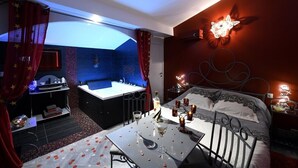 A hotel room with a large bed, a sitting area with a table, and a separate bathroom with a bathtub. - Suite Rouge Passion avec jacuzzi privatif en Provence (Plan-d'Orgon)