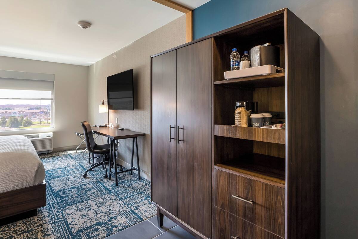A hotel room with a bed, a desk, a chair, a wardrobe, and a television.