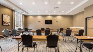 Une salle de conférence équipée de plusieurs tables et chaises, d’une grande fenêtre et d’un téléviseur fixé au mur.