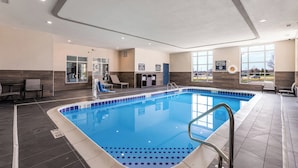 A modern indoor swimming pool with clear water, a tiled floor, and a view of the outside through large windows.
