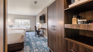 A hotel room with two beds, a desk, a chair, a TV, and a wardrobe with shelves.