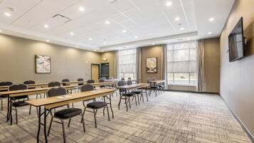 A conference room with multiple tables and chairs, large windows with curtains, and a ceiling with recessed lighting.