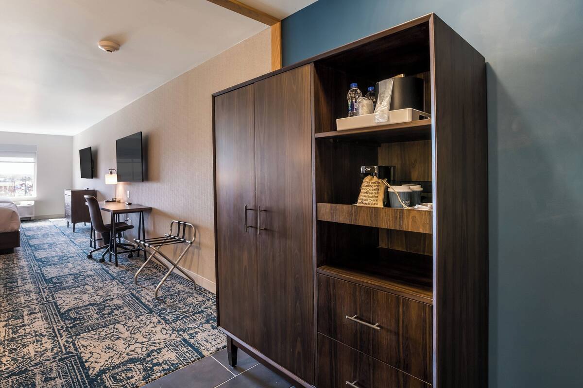 A hotel room with a large wardrobe, a desk with a chair, a bed, and a TV mounted on the wall.