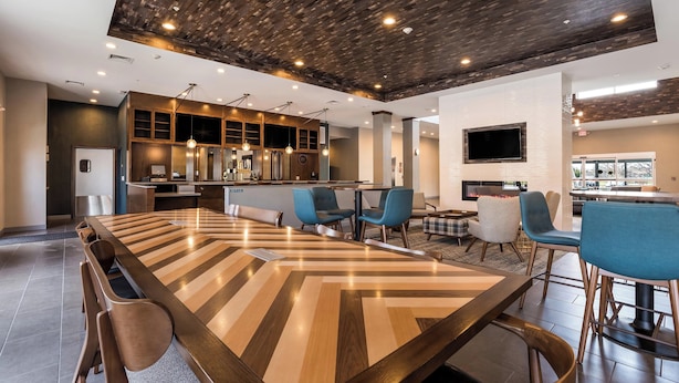 A modern dining area with a long wooden table, blue chairs, and a kitchen in the background.