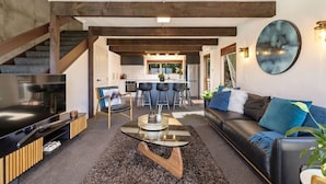 A modern living room with a TV, sofa, and coffee table, leading to a kitchen and dining area.