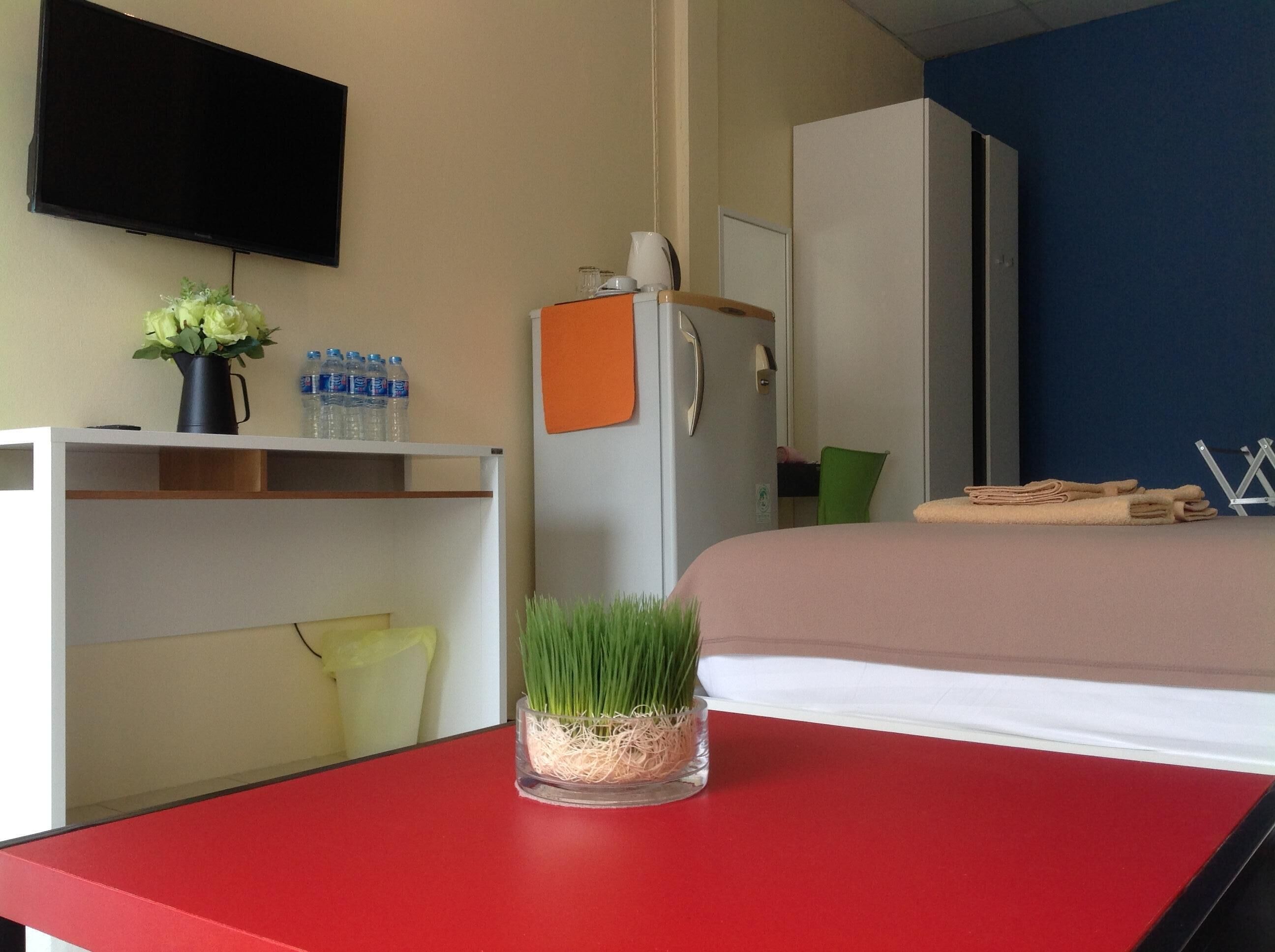 A hotel room with a bed, a desk with a vase of flowers, a water bottle, and a television on the wall.