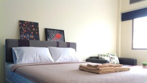A neatly made bed with a brown bedspread, white pillows, and a stack of folded towels. There are two framed artworks on the wall above the bed. - Phuket Town Budget Lodge AirconRoom1+Washer (Phuket)