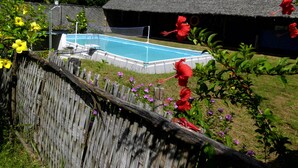 A swimming pool surrounded by a wooden fence, with a thatched-roof building and lush greenery in the background. - Villa Tambatra (Mahavelona)