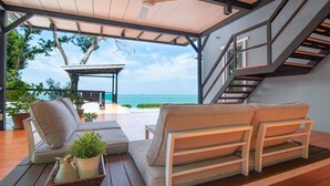 Ein zeitgemäßer Außenbereich mit einer Couch, einem Tisch mit Pflanzen und Blick auf das Meer.