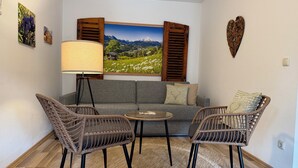 Een woonkamer met een bank, twee rieten fauteuils, een salontafel, een vloerlamp en een groot landschapsprent.
