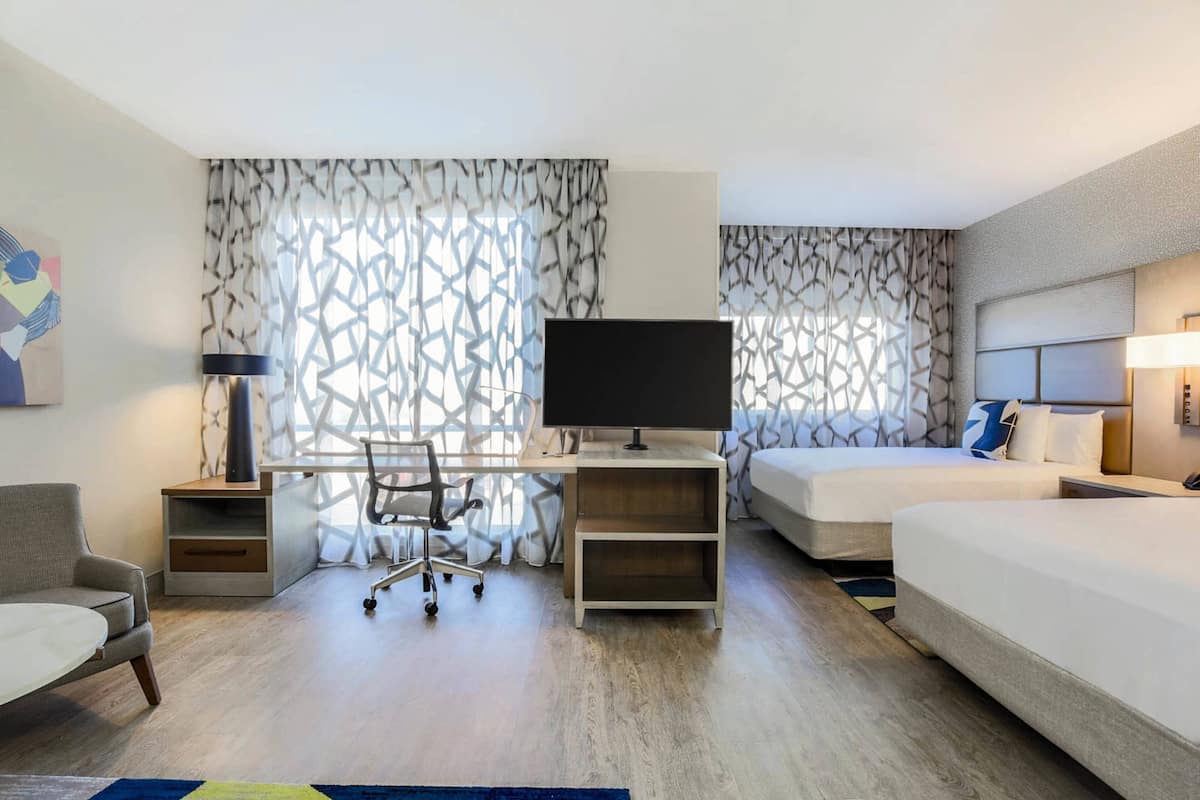 A hotel room with a desk, two beds, a chair, and a TV.