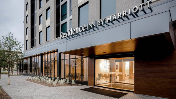 En modern hotellfasad med stora fönster och en skylt med texten ”Residence Inn by Marriott”.