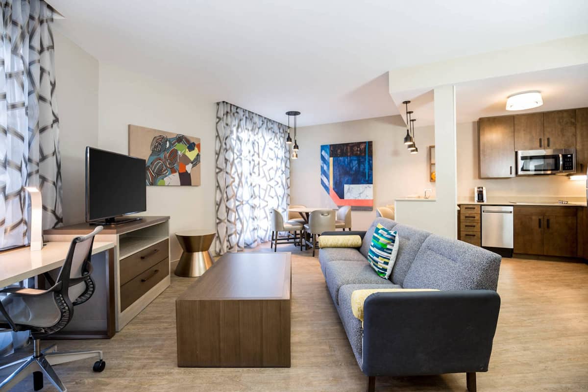 A modern living room with a sofa, coffee table, TV, and a kitchen area with a microwave.