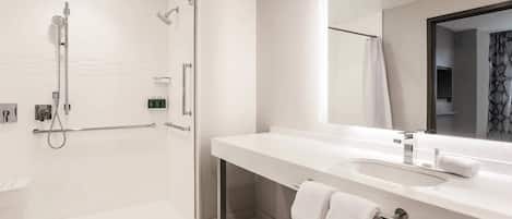 A modern bathroom with a walk-in shower, a large mirror, and a white sink.