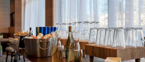A buffet setup with various food items and beverages, including a large pot of soup, bottles of wine, and an assortment of glasses.