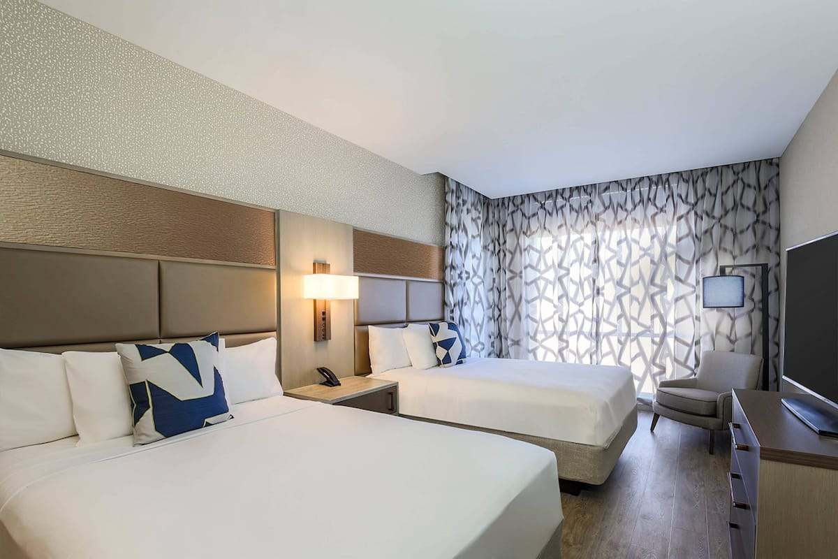 A hotel room with two beds, a desk, a chair, and a TV.