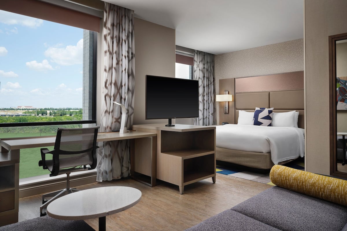 A hotel room with a bed, desk, chair, TV, and a view of the outdoors.