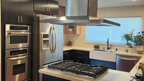 Een moderne keuken met roestvrijstalen apparatuur, een centraal kookeiland met gasfornuis en donkere kastjes.