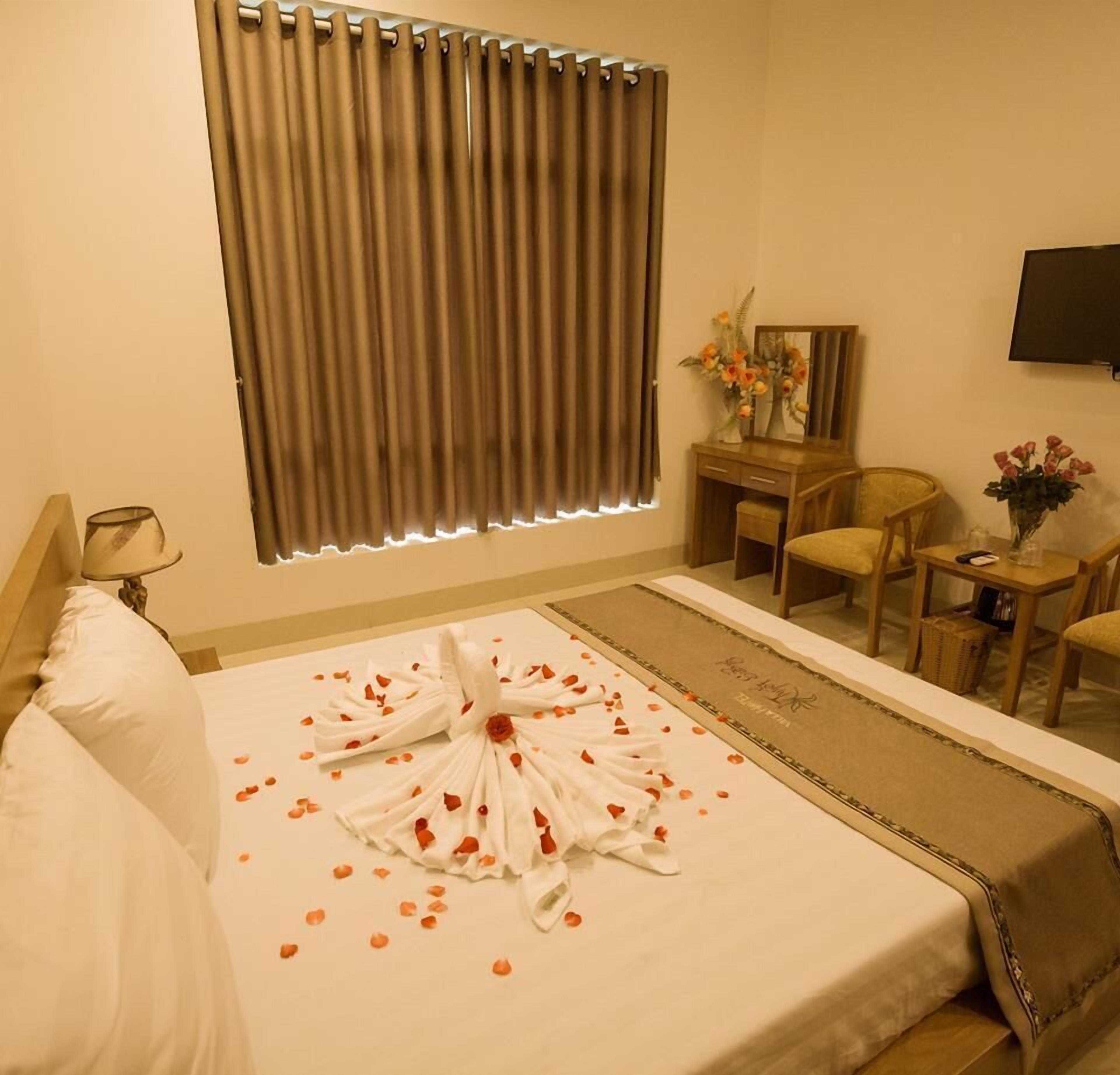 A hotel room with a neatly made bed, a desk with a mirror, a chair, and a television on the wall.
