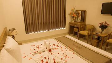 A hotel room with a neatly made bed, a desk with a mirror, a chair, and a television on the wall.