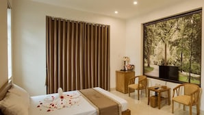 A hotel room with a bed, a desk, a chair, a television, and a large window with a forest view.