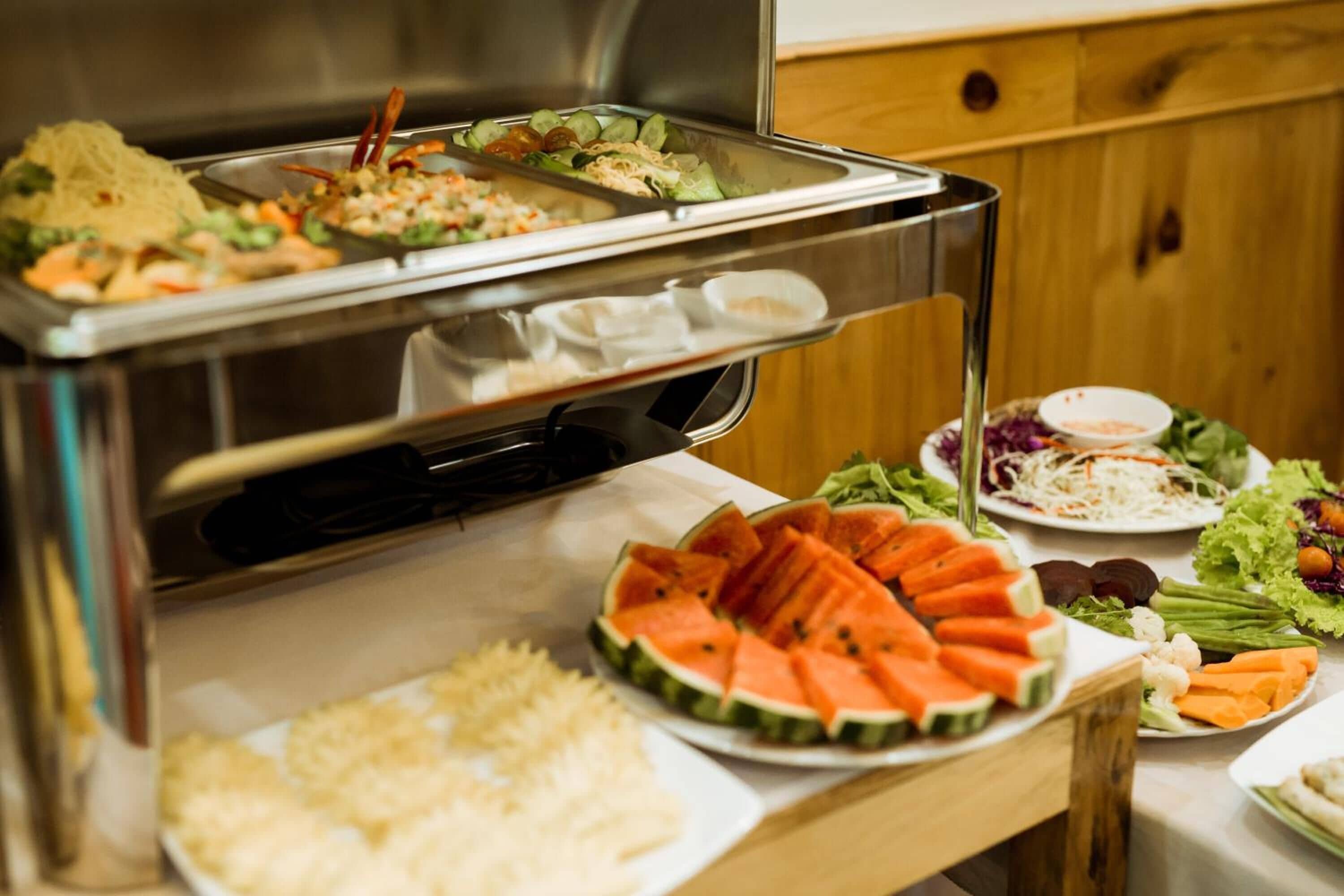 A buffet with various food items including watermelon slices, salads, and rice.