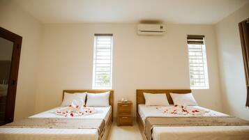 A hotel room with two beds, a small bedside table, an air conditioning unit, and two windows with blinds.