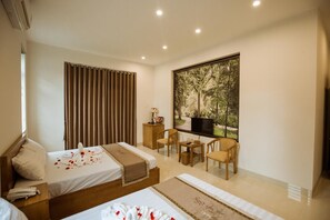 A hotel room with a bed, a desk, a chair, a window with a view of trees, and a television.