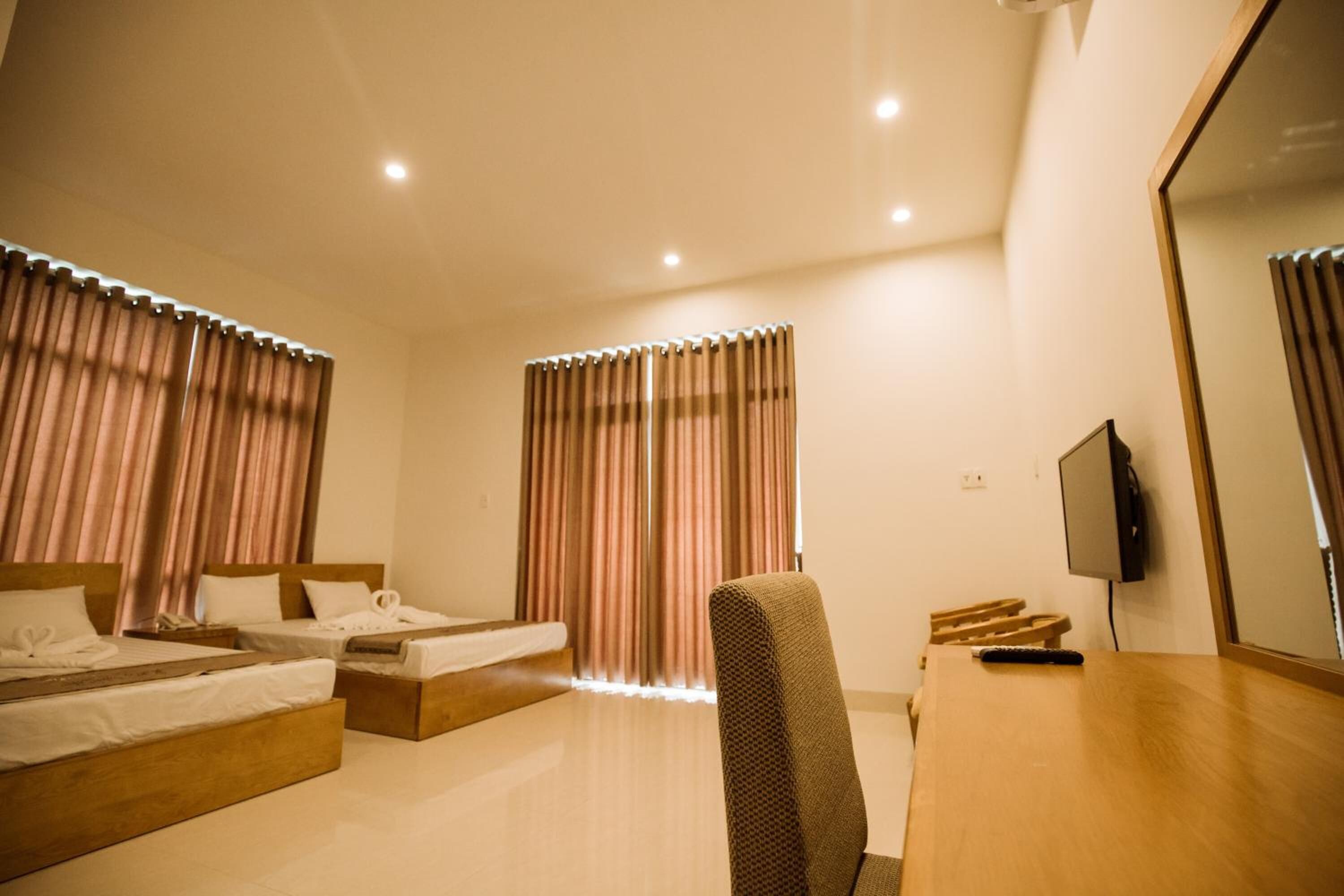 A hotel room with two beds, a desk, a chair, a TV, and curtains.