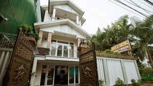 A two-story hotel with a balcony, a signboard, and a well-maintained lawn.
