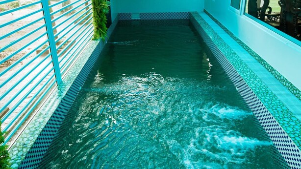 A swimming pool with a blue tiled edge, surrounded by a blue railing and a staircase leading to a covered area.