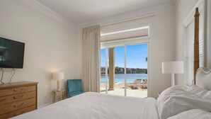 Ein Hotelzimmer mit einem großen Bett, einem Fernseher, einer Lampe, einem Sessel und Blick auf Strand und Meer.