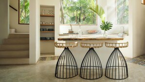 Une cuisine avec une fenêtre donnant sur un jardin tropical, une table en bois avec des tabourets et un escalier.