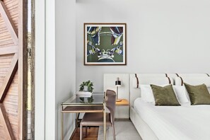 A modern bedroom with a bed, a desk, and a chair. There is a framed artwork on the wall.